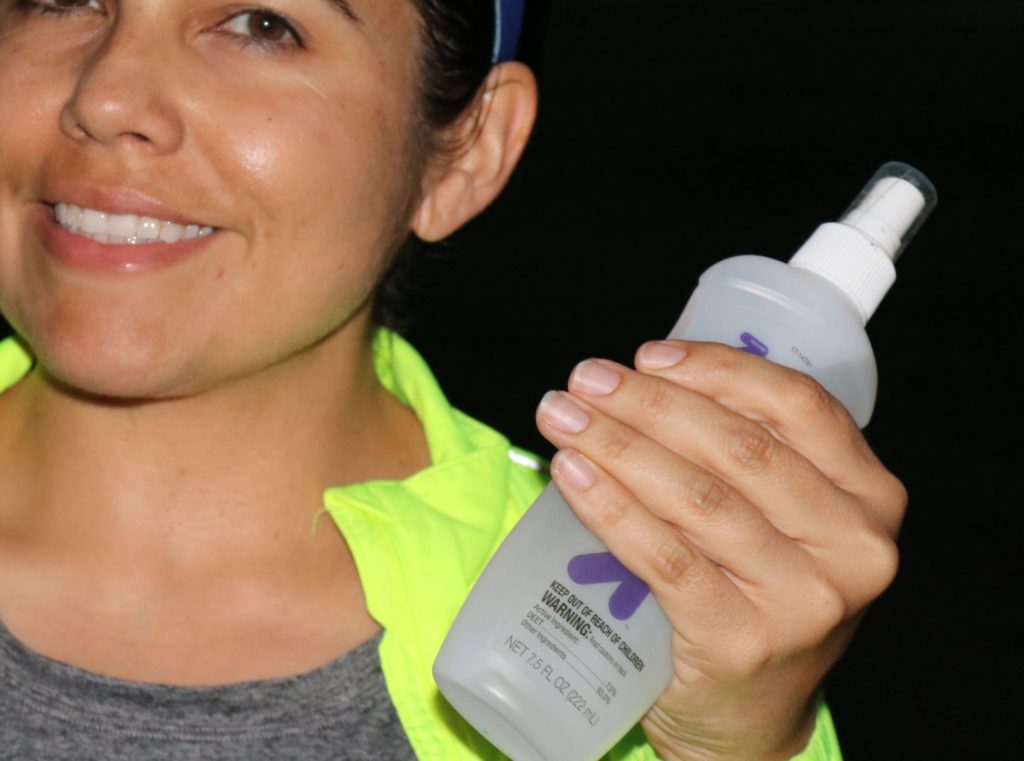 a woman smiling and holding a bottle of insect repellent 