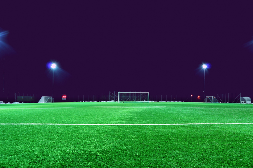 a picture of a soccer field at night with lights on.
