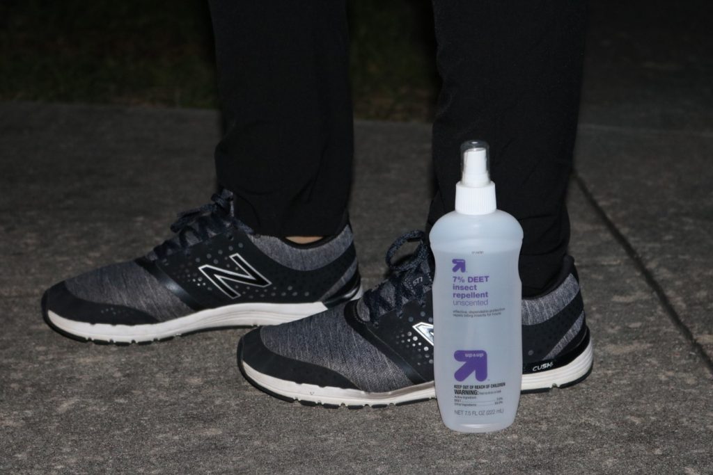 a woman in pants and sneakers standing next to a bottle of insect repellent