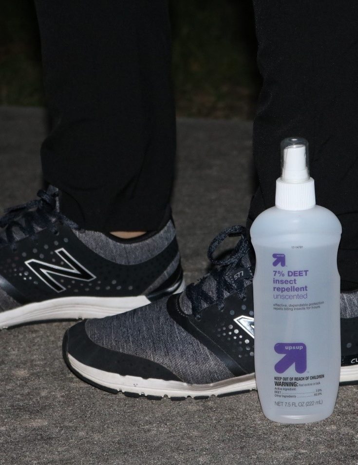 a woman in pants and sneakers standing next to a bottle of insect repellent